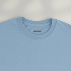 Gros plan du col et de l’étiquette du T-shirt Rivières & Falaises couleur Light Blue sur fond studio gris chaud uniforme