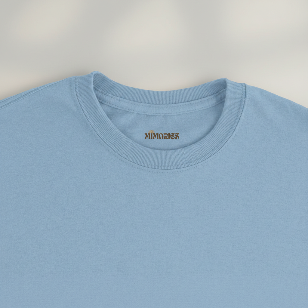 Gros plan du col et de l’étiquette du T-shirt Rivières & Falaises couleur Light Blue sur fond studio gris chaud uniforme